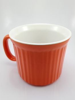 Orange heavy duty mug with handle and ridges use to pour liquid content and soup