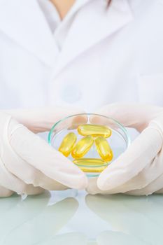 Close up Scientist hands putting in nitrile latex gloves holding Omega 3 capsule in labcoat wearing nitrile gloves, doing experiments in lab