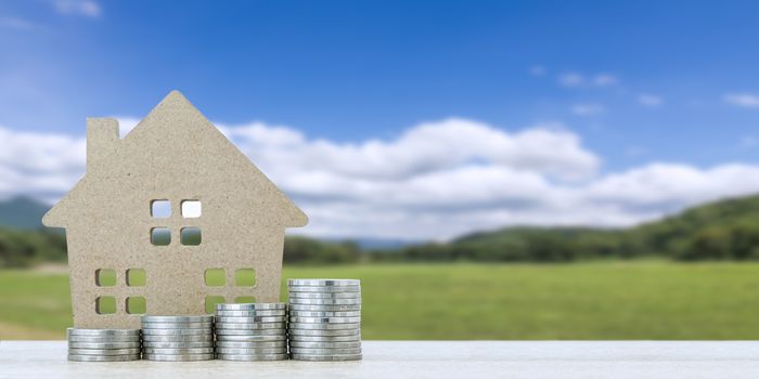 House model and stack of coins on table with landscape back background for finance and banking concept