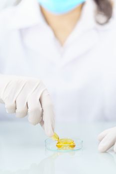 Close up Scientist hands putting in nitrile latex gloves holding Omega 3 capsule in labcoat doing experiments in lab