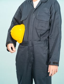 Worker standing in blue coverall holding yellow hardhat isolated on blue background
