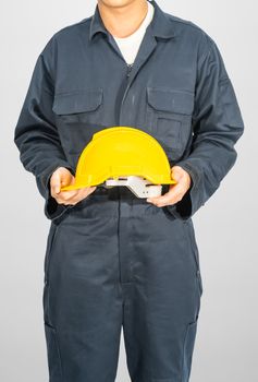 Worker standing in blue coverall holding yellow hardhat isolated on gray background
