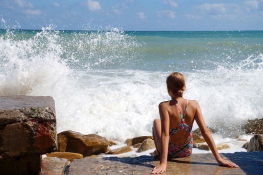 teenage girl sitting on a sandy beach in sea white foam.