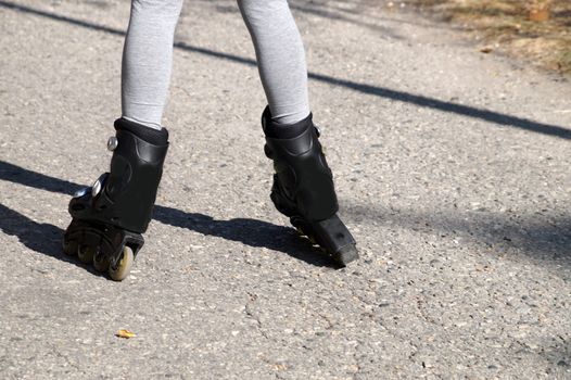 childrens feet in roller skates standing uncertainly on the road, rear view.