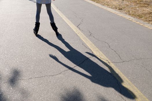 a shadow on the asphalt from a roller-skating girl.