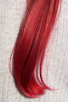 strand of dyed red female hair on a light background close-up