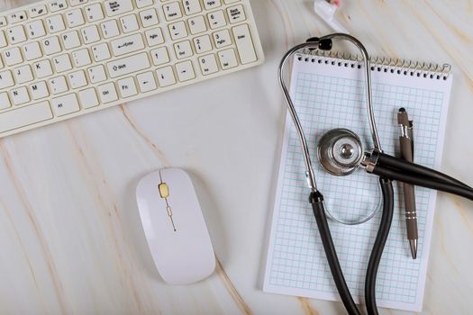 Modern medical office working with computer keyboard on stethoscope over notebook, pen