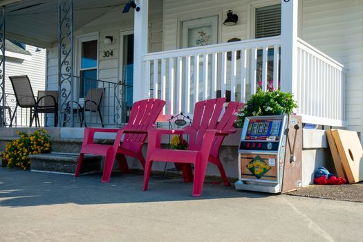 The Front of a Beach House With Two Red Lawn Chairs and a Slot Machine Next to Them