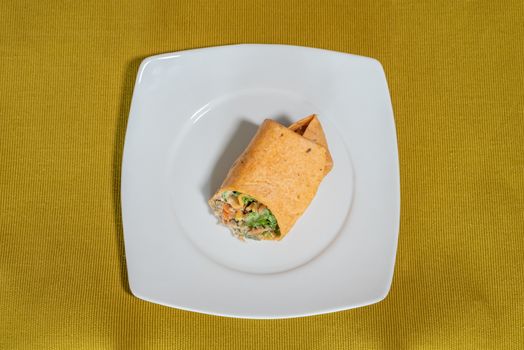 Vegetarian wrap served on a white plate resting on a mustard-colored table runner, food photography depicting a tacos roll stuffed with vegetables and tofu