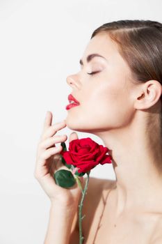 Woman with rose sniffs a flower with her eyes closed bright makeup light background