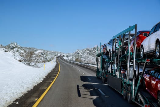 Truck trailer transports new cars rides on highway road with snow covered landscape in the mountains