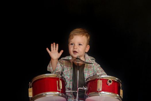 Two year caucasian boy is Playing Drum Set Isolated on Black Background.