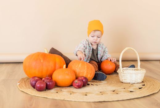 A little kid sits among pumpkins in an autumn photo zone in the studio to celebrate thanksgiving day. Celebrations concept