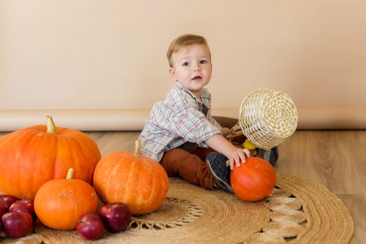 A little kid sits among pumpkins in an autumn photo zone in the studio to celebrate thanksgiving day. Celebrations concept