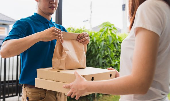 Asian delivery express courier young man giving paper bags fast food and pizza box to woman customer receiving both protective face mask, under curfew quarantine pandemic coronavirus COVID-19
