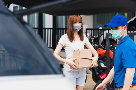 Asian young delivery man courier shopping online give package post box he protective face mask service woman customer receiving box at front home, under curfew quarantine pandemic coronavirus COVID-19