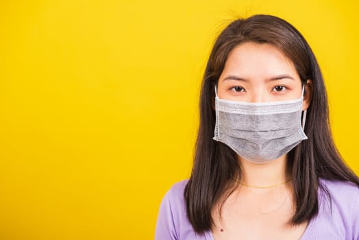 Closeup Asian young teen woman wearing face mask protective against coronavirus, COVID-19 virus or filter dust pm2.5 and air pollution she looking camera studio shot isolated yellow background