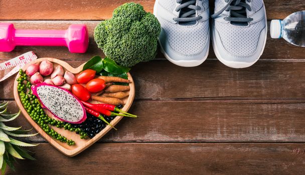 Top view of various fresh organic fruit and vegetable in heart plate and sports shoes, dumbbell and water, studio shot on wooden gym table, Healthy diet vegetarian food concept, World food day