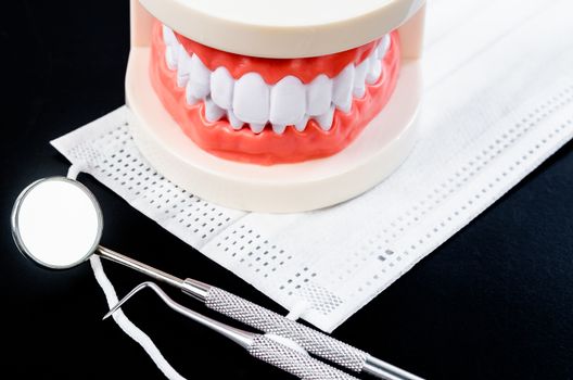 Set of metal Dentist's medical equipment tools with model teeth on black background.