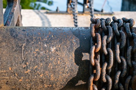 Rusting iron chains are wrapped around a large metal spool, visibly continuing suspended in the background.