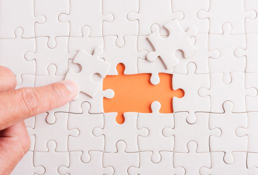 Top view flat lay of hand-holding last piece white paper jigsaw puzzle game last pieces put to place for solve problem complete mission, studio shot on an orange background, quiz calculation concept