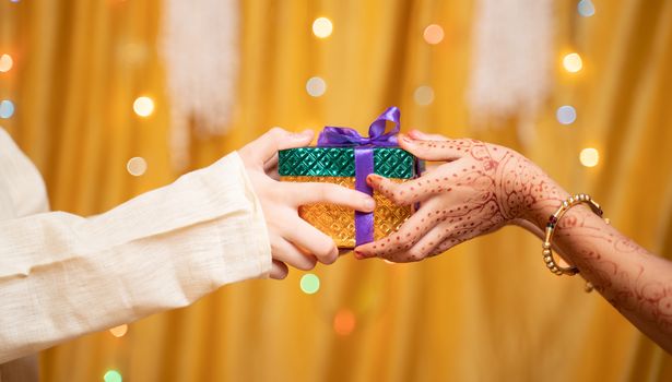 Close up of Brother Hands Giving gift to sister during during raksha Bandhan, Bhai Dooj or Bhaubeej Indian religious festival .