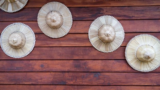 Farmer hat made of palm leaves displays decoration on wood plank wall.
