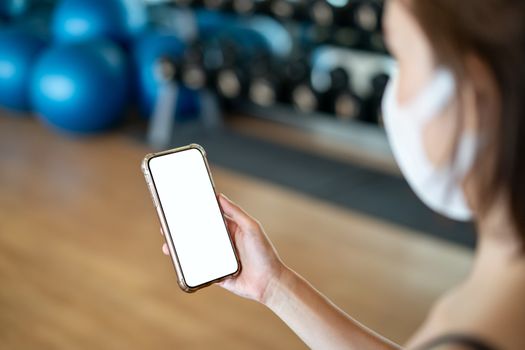 Women wearing mask making holding mockup mobile phone in the gym.