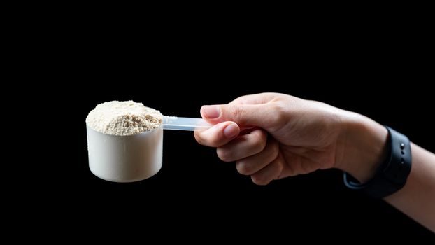 Close up of women hand holding measuring scoop of whey protein preparing protein shake.