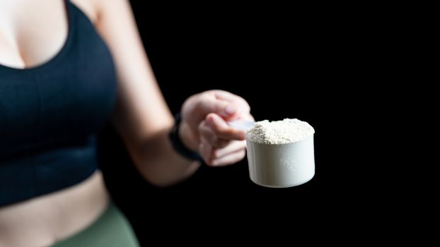 Close up of women hand holding measuring scoop of whey protein preparing protein shake.