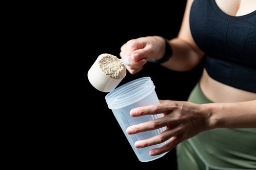 Close up of women with measuring scoop of whey protein and shaker bottle, preparing protein shake.