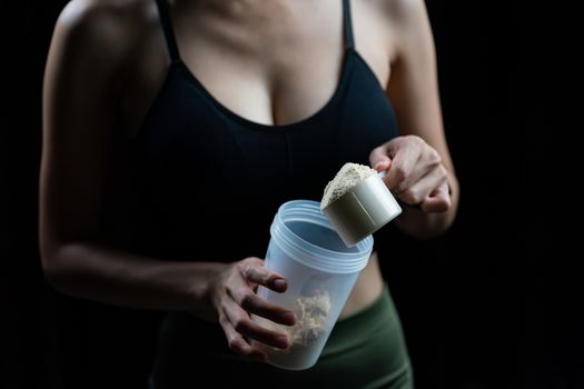 Close up of women with measuring scoop of whey protein and shaker bottle, preparing protein shake.
