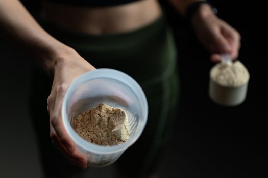 Close up of women with measuring scoop of whey protein, jar and shaker bottle, preparing protein shake.