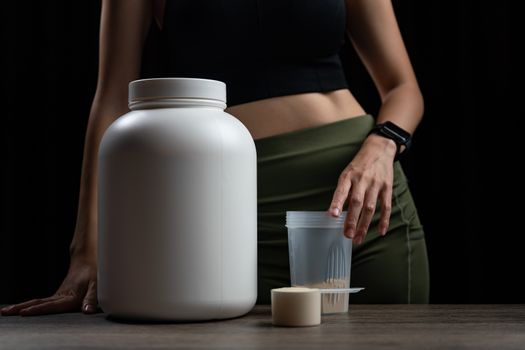 Close up of women with measuring scoop of whey protein, jar and shaker bottle, preparing protein shake.