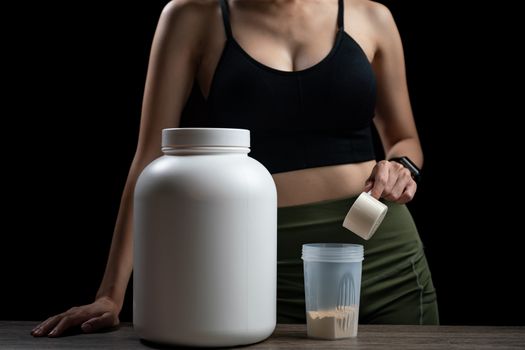 Close up of women with measuring scoop of whey protein, jar and shaker bottle, preparing protein shake.