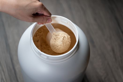 Woman's hands holding measuring scoop of whey protein powder over jar.