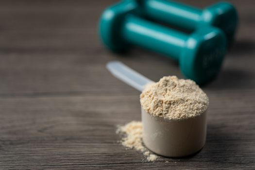 Whey protein powder in scoop and dumbbells. Sports drink, nutrition for muscle growth.