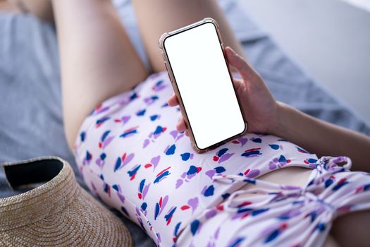Woman in pink swimsuit holding mockup blank mobile phone with white screen on sunbathing bed .