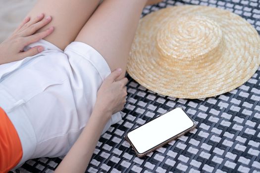 Woman lying on sunbath bed with mobile phone and blank white screen mockup on the beach.