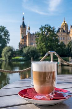 Cup of cappuccino in an outdoor cafe or restaurant on a summer day with a beautiful castle in Schwerin in the background.