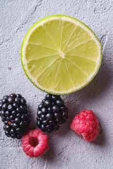 Citrus lime slice, raspberry and blackberry berries, healthy summer fruits on stone concrete background, top view macro