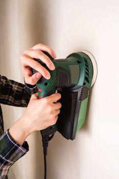 Woman hands holding and working with electric sander to smooth plaster wall surface, room renovation concept