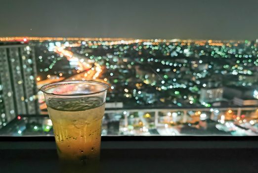 A glass of beer with cityscape from high condominium view at night.