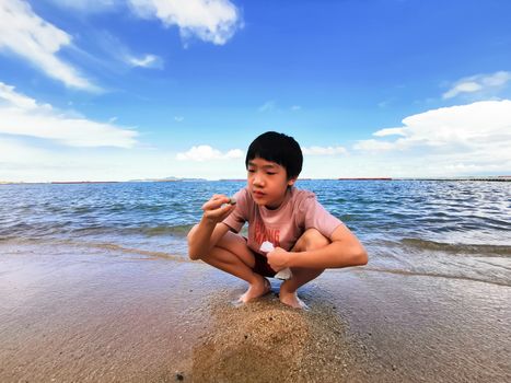 An Asian boy has playing a stone on the beach with blue sky in the morning.
