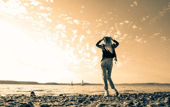 Blonde girl with long hair meets sunrise by the sea