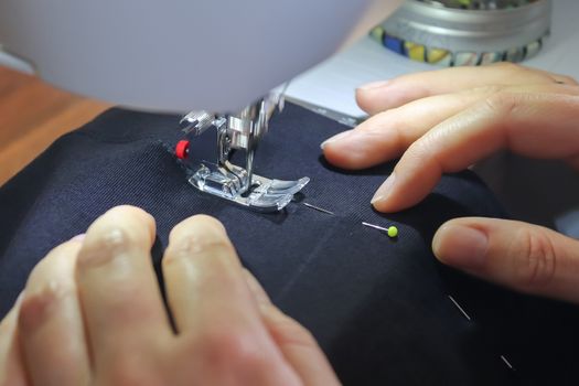 Female hands working at a modern sewing machine with some fabrics and textiles