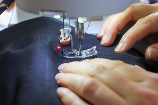 Female hands working at a modern sewing machine with some fabrics and textiles