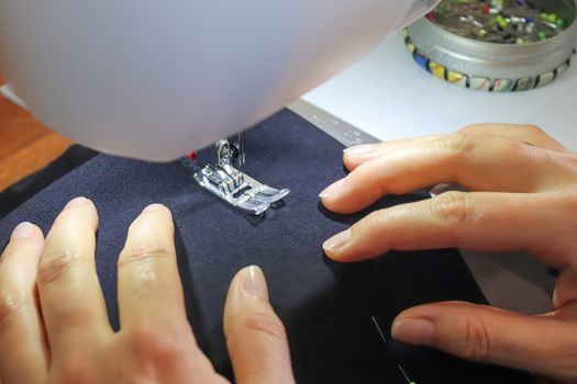 Female hands working at a modern sewing machine with some fabrics and textiles