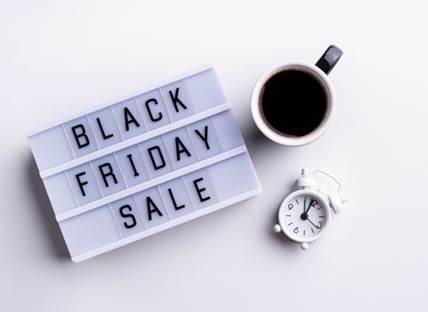 Black Friday Sale words on lightbox with cup of coffee and clock top view flat lay on white background with copy space