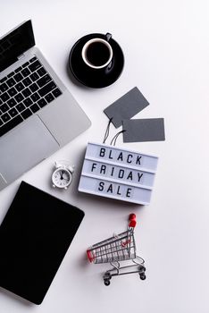 Black Friday Sale words on lightbox with cup of coffee, laptop and clock top view flat lay on white background with copy space